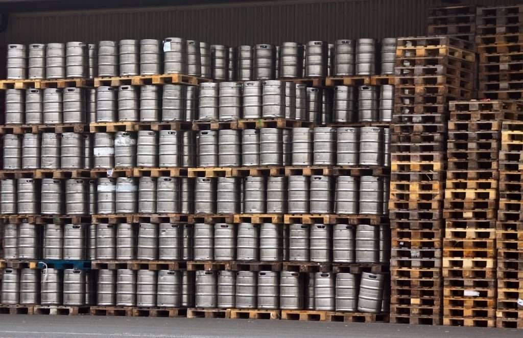 Vários paletes empilhados com barris de metais em cima.