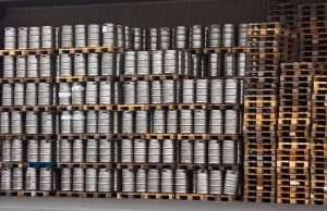 Vários paletes empilhados com barris de metais em cima.